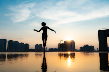 Silhouette of ballerina performing on cityscape and dramatic sunset background. Concept of individuality, creativity and outstanding © Hladchenko Viktor