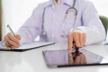 A doctor with a clipboard writing on paper and a tablet at the desk