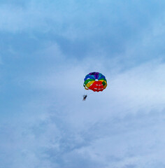 Two men are sailing on a colorful and bright parachute against the blue sky. Copy space