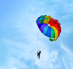 Two men are sailing on a colorful and bright parachute against the blue sky. Copy space