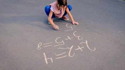 The child writes math on the pavement. Selective focus.