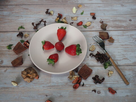 Strawberry plate with wooden fork on vintage white table with dry leaves