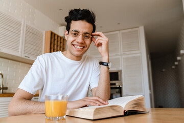Fototapeta na wymiar Young hispanic man reading a book while having breakfast