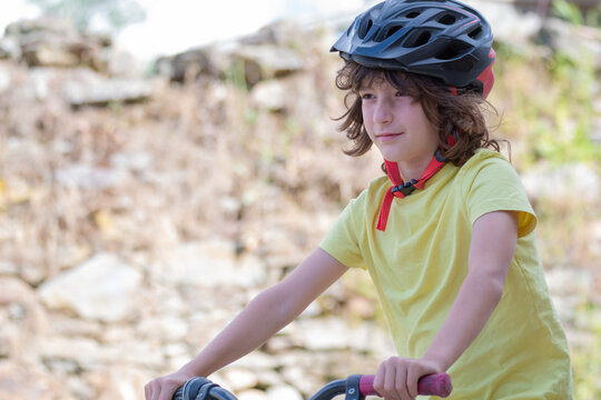 smiling boy in red helmet and yellow t-shirt has fun riding bike on sunny day