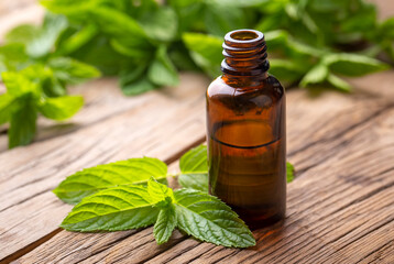 Glass bottle of peppermint essential oil with fresh green mint leaves, mint oil