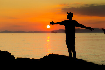 A young boy in a pool enjoying the sunset. Human silhouette over the setting sun.