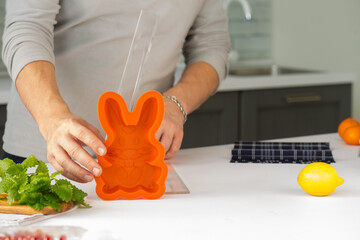 orange silicone mold rabbit for baking cakes, standing behind a man and hands, next to fruits and...