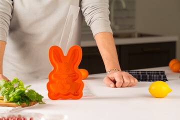 orange silicone mold rabbit for baking cakes, standing behind a man and hands, next to fruits and...