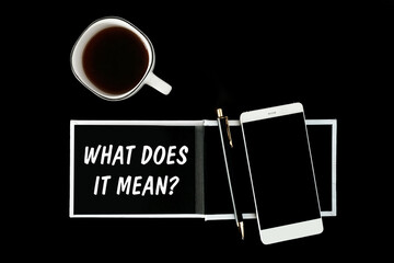 A notebook with black pages, smartphone and a cup of coffee on a black background. The inscription What Does It Mean