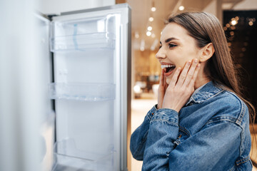 Fototapeta na wymiar Young attractive woman choosing refrigerator in hypermarket
