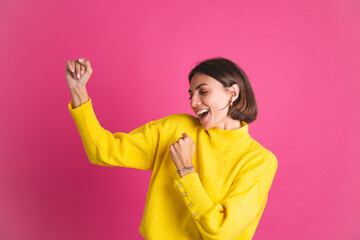 Beautiful woman in bright yellow sweater isolated on pink background happy excited dancing moving smile