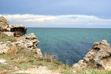 Sea view from the shore with large stones, green grass in summer.