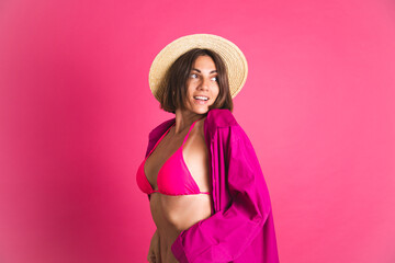 Beautiful fit tanned sporty woman in bikini straw hat and shirt on pink background