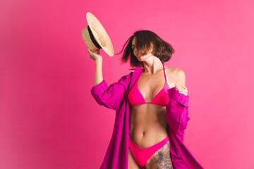 Beautiful fit tanned sporty woman in bikini straw hat and shirt on pink background