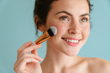 Half-naked brunette woman smiling while using cosmetic brush