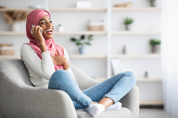 Cheerful Black Muslim Woman In Hijab Talking On Mobile Phone At Home