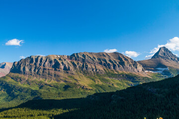 partially snow covered jagged mountain peaks of Glacier National park near Iceberg Lake trail during summer.