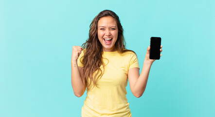 young pretty woman feeling shocked,laughing and celebrating success and holding a smart phone