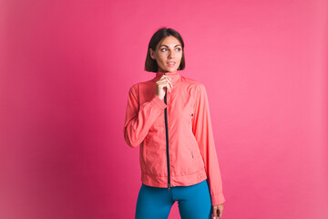 Young fit woman in sport wear jacket on pink background