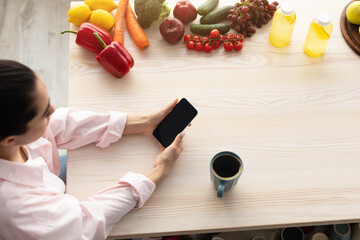 Woman using smartphone with empty screen for mockup in kitchen