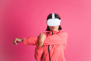 Young fit woman in sport wear jacket and virtual reality glasses stretching herself on pink background