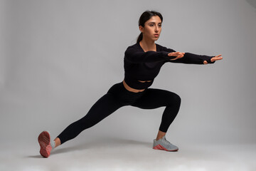 Fit brunette doing bodyweight side lunges on grey background