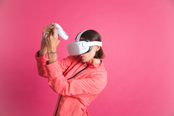Young fit woman in sport wear jacket and virtual reality glasses playing boxing fight games on pink...