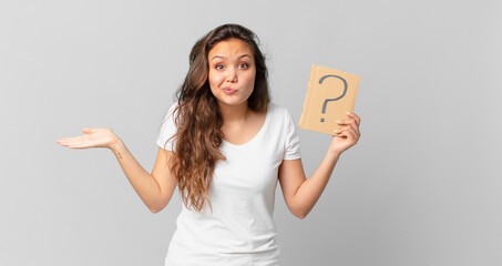 young pretty woman feeling puzzled and confused and doubting and holding a question mark sign