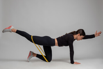Woman doing Dandayamana Bharmanasana with resistance band on grey background