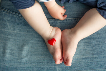 Kid feet with red heart. Baby legs on denim background. Children protection, parenthood and family concept.