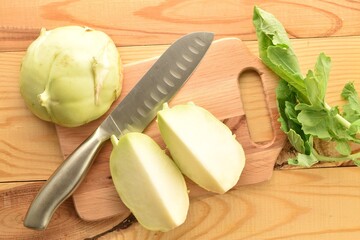 Several slices of kohlrabi cabbage with a metal knife on a wood board, close-up, top view.