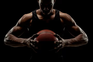 Schilderijen op glas Basketball player holding a ball against black background. Serious concentrated african american man © Nikola Spasenoski