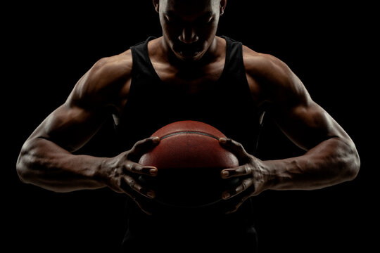 Basketball player holding a ball against black background. Serious concentrated african american man