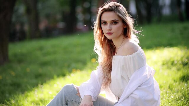 Portrait of young beautiful woman sitting on grass, on green background summer nature. Calm girl enjoy smile and relax in spring city air.