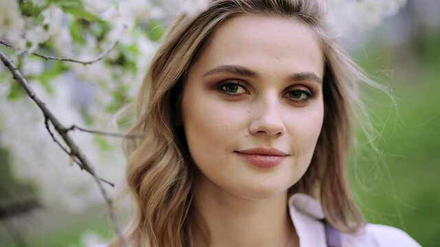 Happy Beautiful girl in Garden with blooming trees. Portrait of young beautiful blonde woman in the flowered garden in the spring time