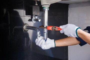 Plumber fixing white sink pipe with adjustable wrench.