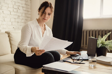Middle aged business woman working at home with documents using laptop
