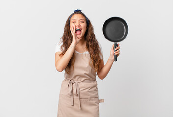young pretty woman feeling happy,giving a big shout out with hands next to mouth chef concept and holding a pan
