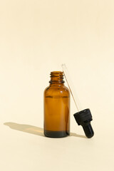 A glass bottle with a pipette for essential oil, lotion or serum on a pastel beige background. Dark amber glass bottle. Layout of the beauty salon branding