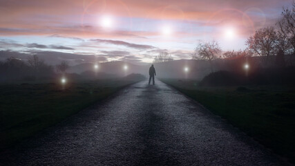 A UFO concept of glowing orbs, floating above a misty winters road just after sunset. With a...