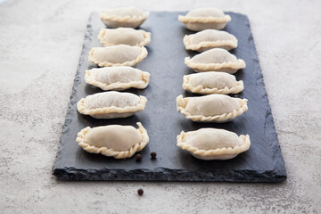 The raw dumplings are laid out on a black slate stone board.