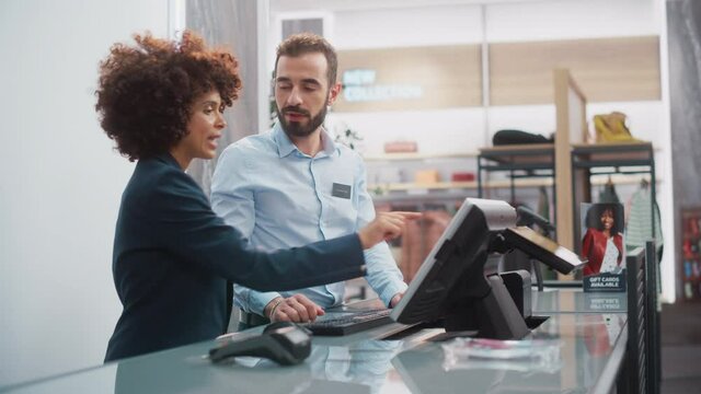 Clothing Store Checkout Cashier Counter: Female Retail Sales Manager Explaining to New Male Assistant Employee Everything He Needs to Know About Working at Fashionable Shop with Stylish Brand Designs.