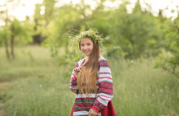 A girl in a Belarusian folk costume stands in the forest with a wreath on her head and flowers in her hands. The concept of the traditions of the Slavic people