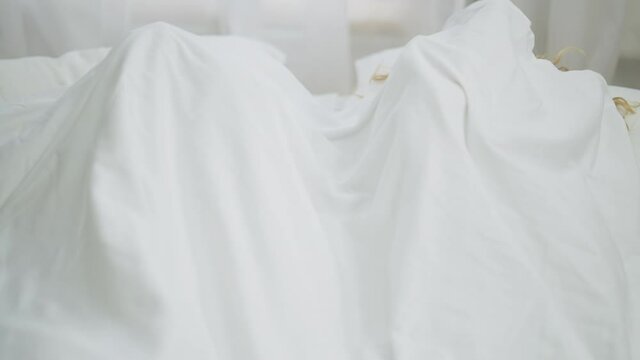 Young happy millennial couple hiding under white blanket cuddling lying in bed. Smiling African American man and Caucasian woman having fun in bedroom in the morning. Love and bonding