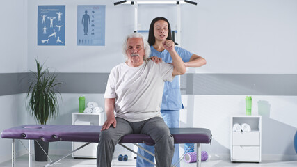 Rehabilitation therapist stretching arm of elderly man