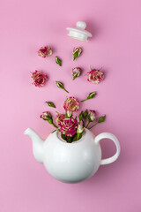 Creative layout with flowers flying out of the teapot. Kettle and roses. Pink background. View from above. Flat lay. Tea time concept.