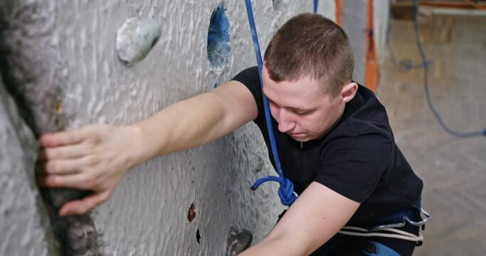 A young guy climbs on an artificial wall to study climbs a wall in the insurance hard to overcome obstacles physically overcomes climbing indoors