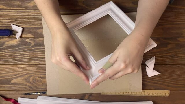 Women's hands gluing frames made of styrofoam. Interior details made of moldings. Wooden table, hot glue and cardboard on background. Designer's workspace. Diy handicraft process.