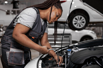 Confident Caucasian Female Mechanic is Working With Car In Car Service. Woman in Overalls is Working on Usual Car Maintenance, Using Ratchet. Modern Clean Workshop with Cars.