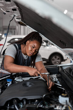 Beautiful Caucasian Female Mechanic is Working With Car In Car Service. Woman in Overalls is Working on Usual Car Maintenance, Using Ratchet. Modern Clean Workshop with Cars.